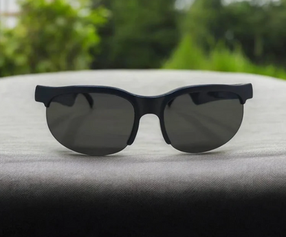 Black sunglasses with dark lenses resting on a gray textured surface with a blurred green outdoor background.